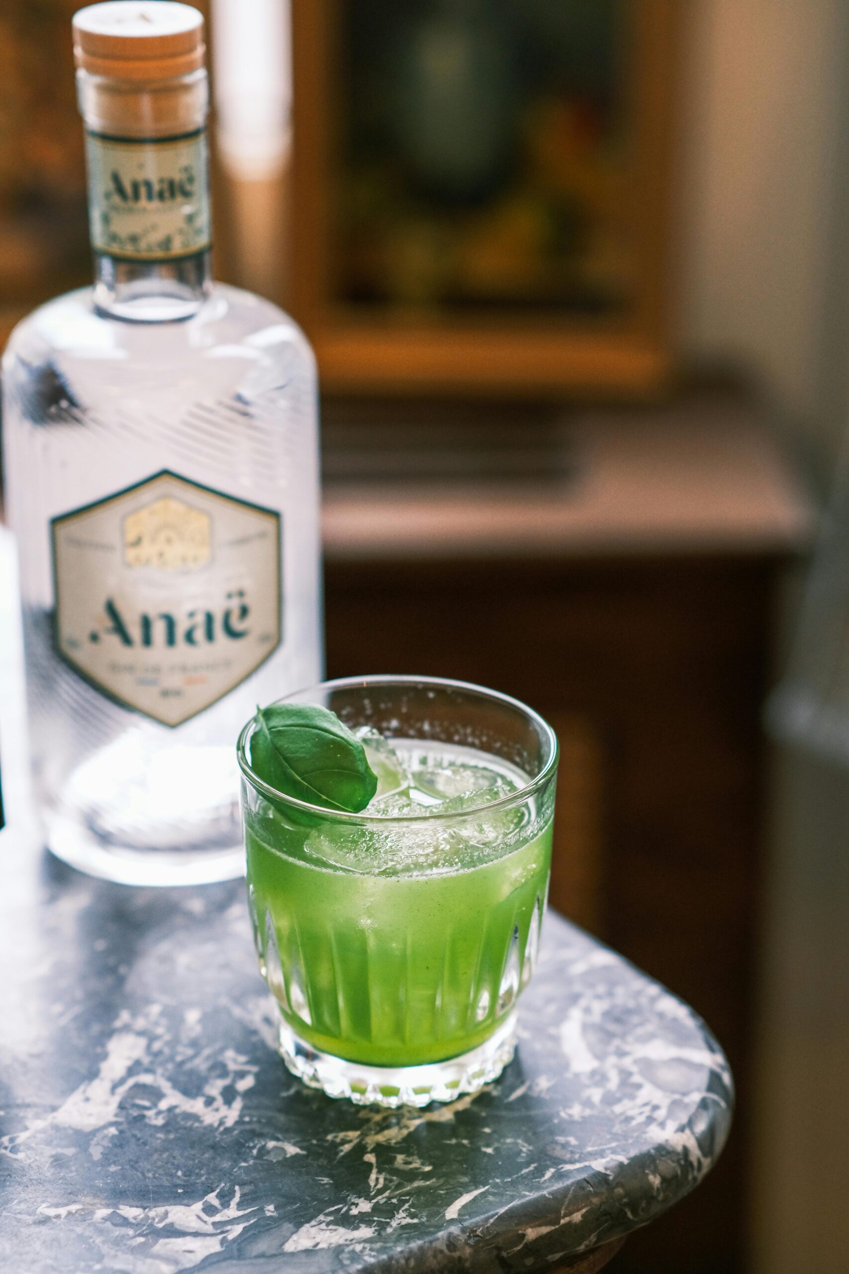 Elegant green gin cocktail with basil garnish on marble surface, perfect for a refreshing drink vibe.